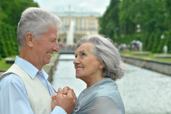Senior couple holding hands and smiling at each other beside a formal garden canal