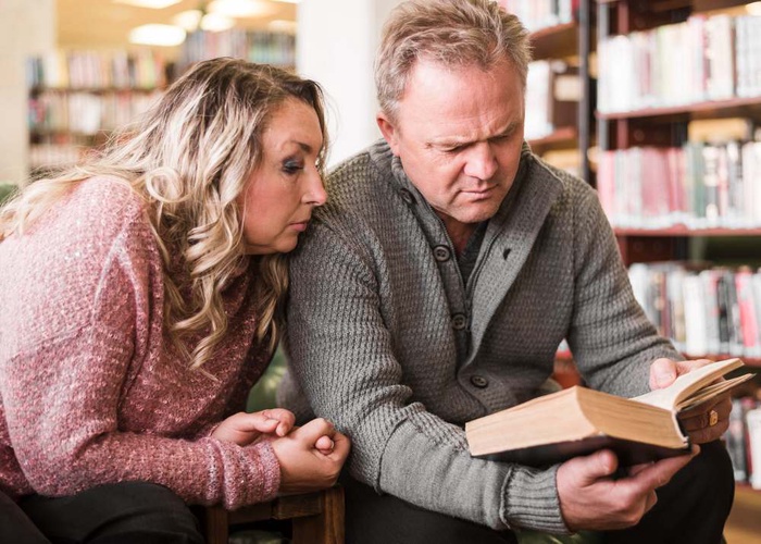 A mature couple reading an open book together in a library