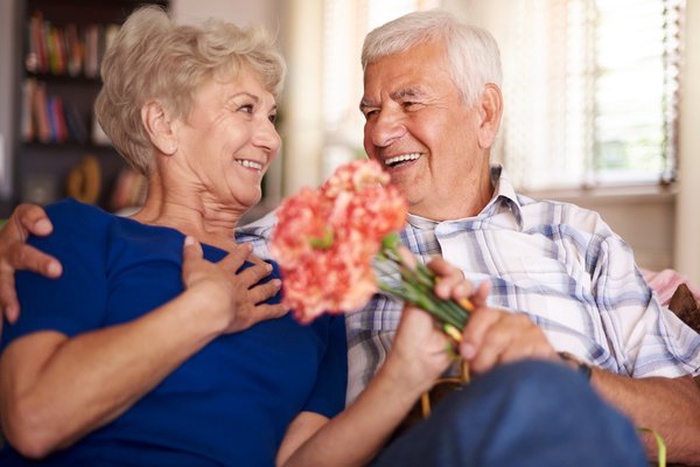 Senior couple smiling together while sharing flowers at home