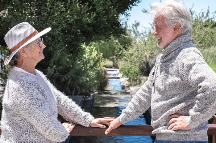 Senior couple holding hands and talking beside a tree-lined waterway in Bedford, England