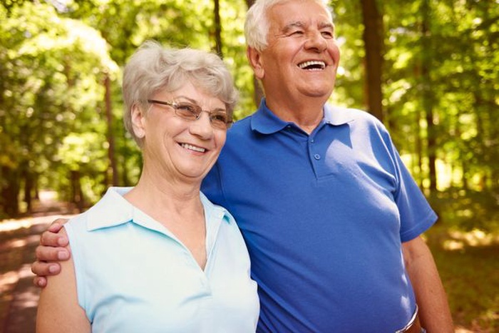 Older couple smiling together on a wooded walking trail.