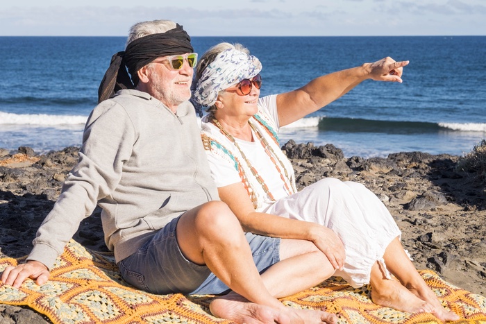 `Older couple relaxing together by the ocean and enjoying the coastal view.`