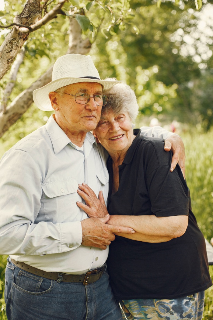 Older couple standing close together beneath leafy trees