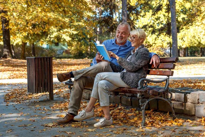 Senior couple reading together on a park bench surrounded by autumn leaves
