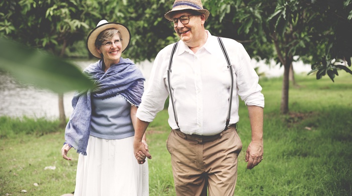 A mature couple enjoys a relaxed walk through a green outdoor setting, reflecting companionship and an active lifestyle for singles over 50 in Thousand Oaks.