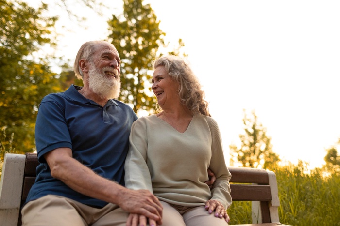 Older couple smiling together on a park bench in warm evening light