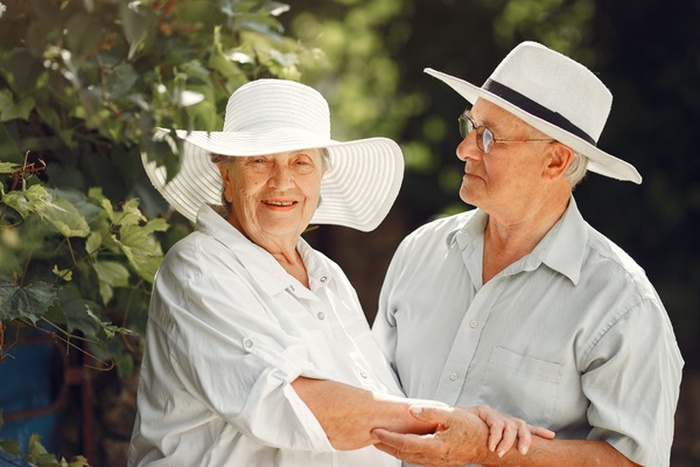 Older couple wearing white sun hats and holding hands outdoors