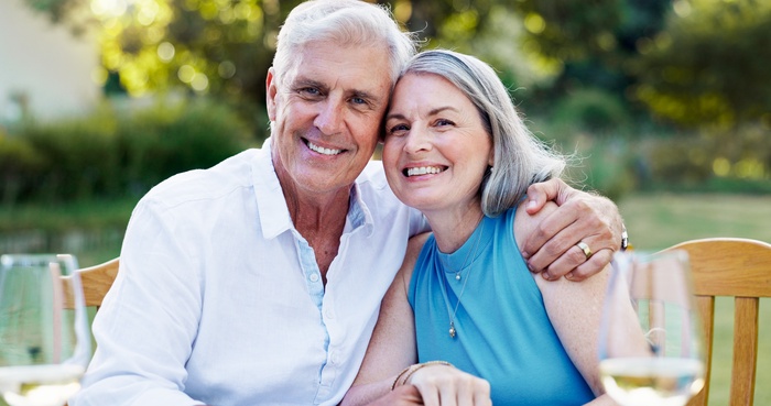 Smiling senior couple sitting close together outdoors in a sunny garden, enjoying a relaxed moment together.
