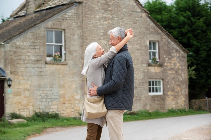 Older couple embracing outside a stone cottage in Paisley, Scotland