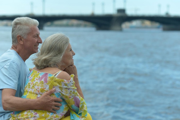 Older couple embracing by the waterfront with a bridge in the background in Kingston, Ontario