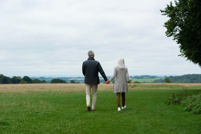 Mature couple walking hand in hand across an open grassy park