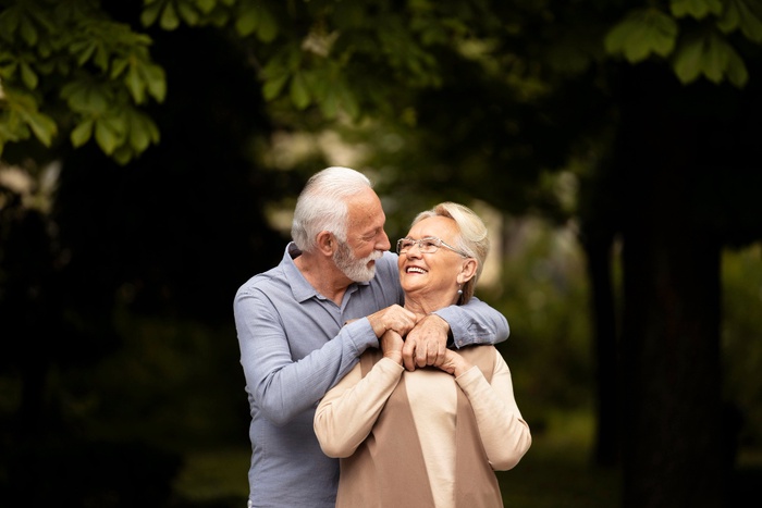 Older couple smiling together in a leafy outdoor setting