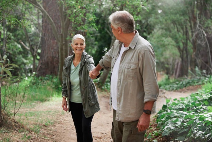 Older couple holding hands while walking along a wooded trail in Fredericton