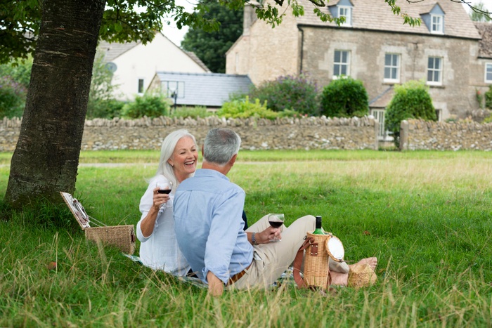 An older couple sharing a relaxed picnic in a leafy outdoor setting