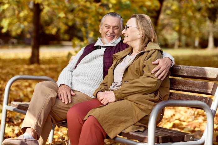 Senior couple relaxing together on a park bench during autumn in Cheltenham, England