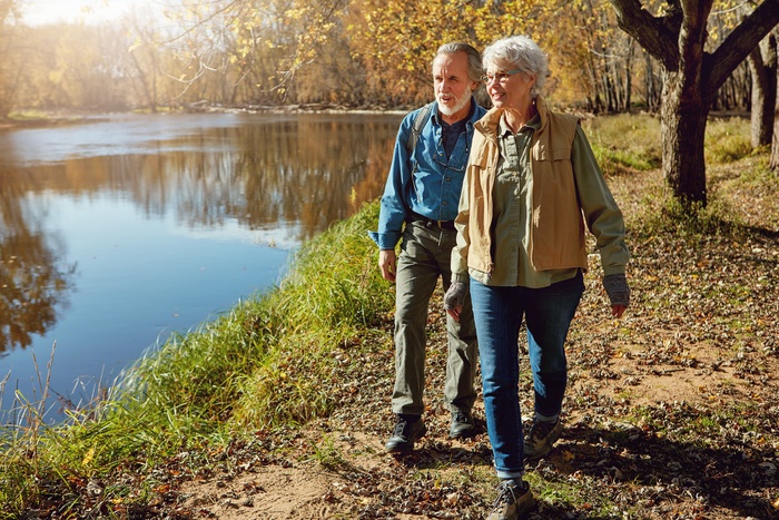 Older couple over 50 enjoying a walk and conversation near a lakeside trail, representing meaningful connections and everyday life after 50