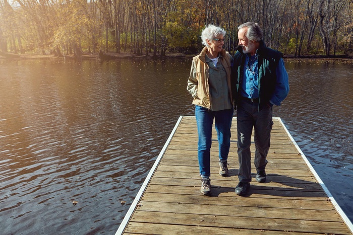 enior couple walking together on a lakeside dock in autumn