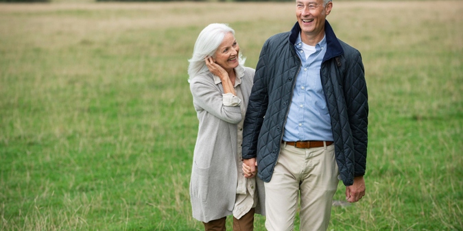 Older couple holding hands while walking through a field