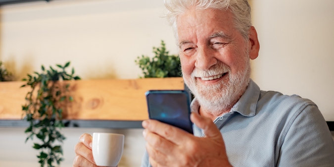 Smiling older man reading his phone over coffee