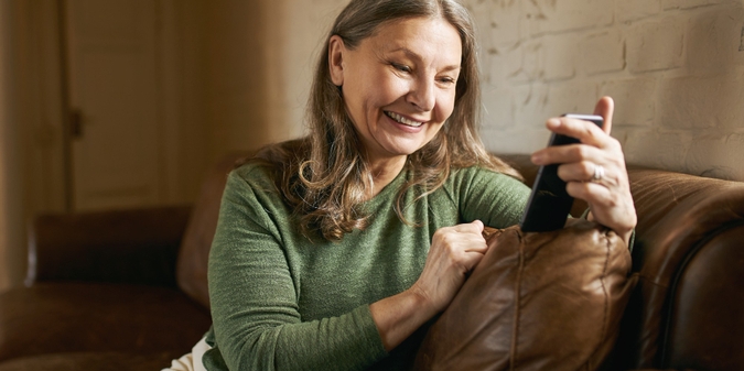 Mature woman smiling at her phone at home