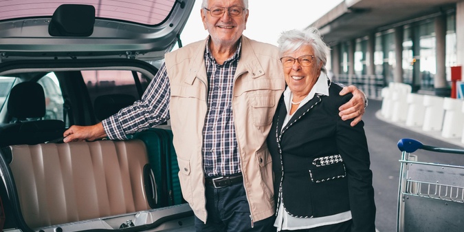 Senior couple standing together beside an open car  复制