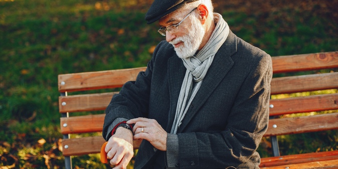 Gray-haired older man sitting on a park bench outdoors